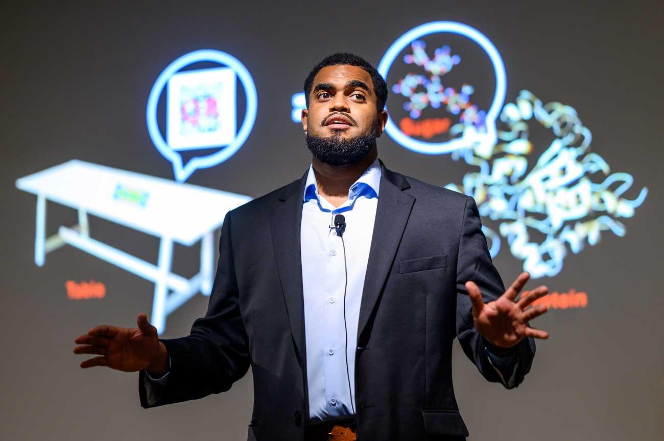 Ruben Hogan speaks in front of graphics on screen.